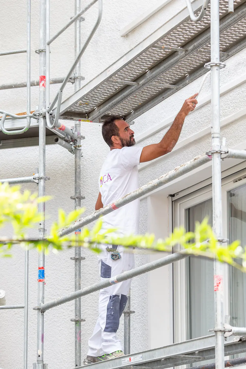 Un homme sur un échafaudage en train de peindre une façade avec minutie et expertise.