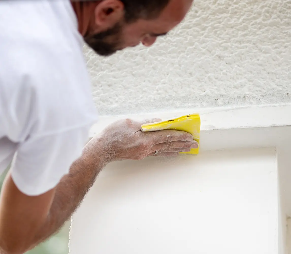 Un homme en train de poncer une façade avec détermination et précision.